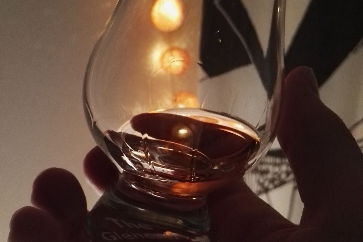 Hand holding a Glencairn glass of whisky, the cover image for our whisky FAQ for Malaysia