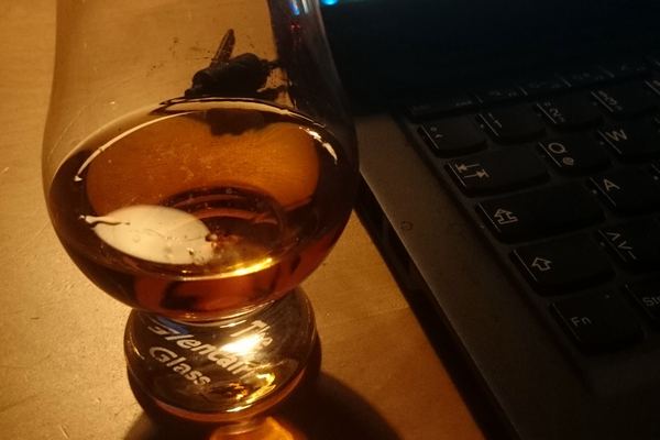 Glencairn glass of whisky glowing by lamp light at home