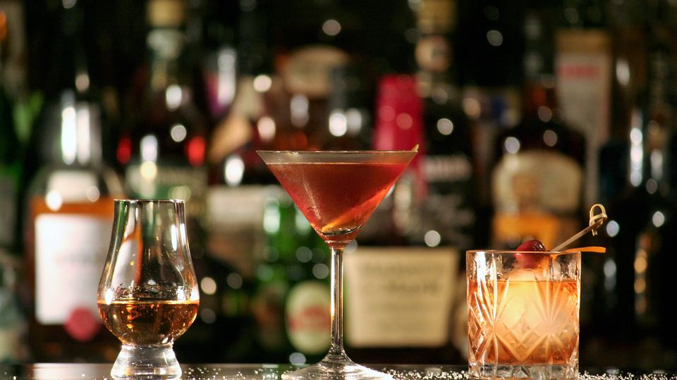 A nosing glass of whisky, a Manhattan in a coupe and an Old Fashioned in a rocks glass on a bar