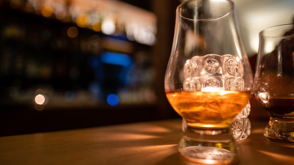 Glass of amber whisky glowing on a bar counter with blurred back-bar bottles